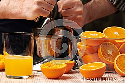 Squeezing an orange with a manual press, close view, making a glass of fresh. Fresh oranges on a wooden table, whole, squeezed and Stock Photo