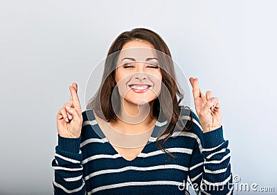 Squint smiling young desiring woman crossing fingers with closed eyes on blue bright background. Girl makes the surprise wish Stock Photo