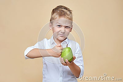 Squinting disheveled little boy beats a green pear Stock Photo