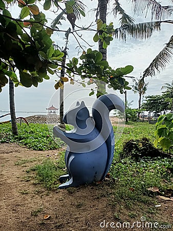 Squirrel statue under a coconut tree on Sanur beach, Denpasar, Bali Stock Photo