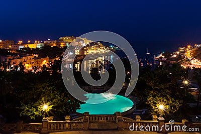 St. George`s Bay seafront lights by night, a blue swimming pool, boats, yachts anchored. St Julian`s, Paceville, Malta. Stock Photo