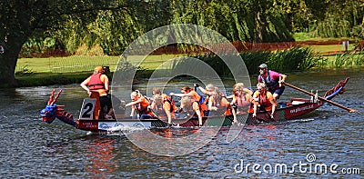 Ladies dragon boat team in orange racing on the river Ouse. Editorial Stock Photo