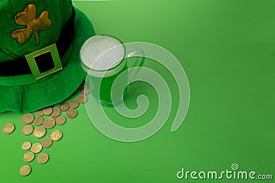St Patrick`s Day green beer with shamrock, pot with gold coins, horseshoe and Leprechaun hat against green background. Stock Photo