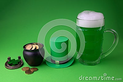 St Patrick`s Day green beer with shamrock, pot with gold coins, horseshoe and Leprechaun hat against green background. Stock Photo
