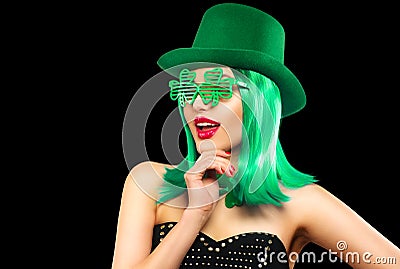 St. Patrick`s Day leprechaun model girl in green hat, funny clover shaped sunglasses, isolated on black background and smiling Stock Photo