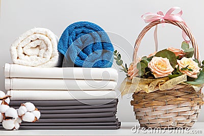 A stack of bed linen sheets bedding rolls of towels. Basket with roses flowers on the table Stock Photo