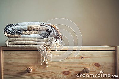 Stack of beige checkered wool blankets on a wooden chest. Stock Photo