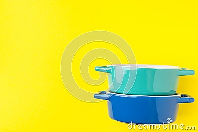 Stack of blue and turquoise ceramic cocottes on bright yellow background. Cooking baking cookware concept Stock Photo