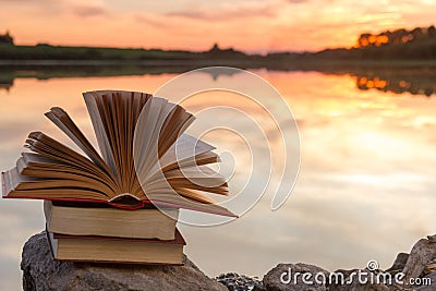 Stack of book and Open hardback book on blurred nature landscape backdrop against sunset sky with back light. Copy space, back to Stock Photo