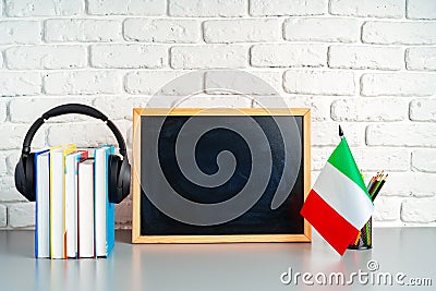 Stack of books, blackboard and flag of Italy on desk. Italian language learning concept Stock Photo