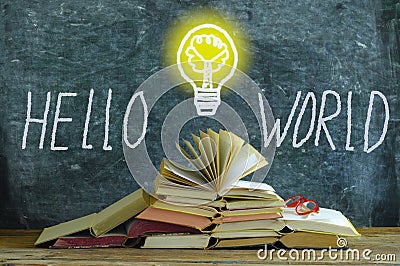 Stack of books in front of a blackboard, drawing of a lightbulb and slogan hello world,knowledge, education and social integration Stock Photo