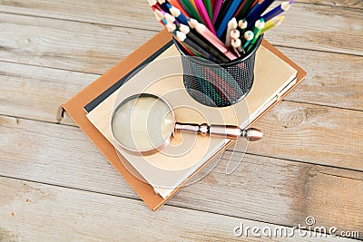On a stack of books in front of a blackboard full of mathematical formulas, a pen holder full of colored pencils and a magnifying Stock Photo