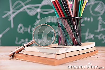 A stack of books in front of a blackboard full of mathematical formulas and a red apple on the books and a pen holder full of colo Stock Photo