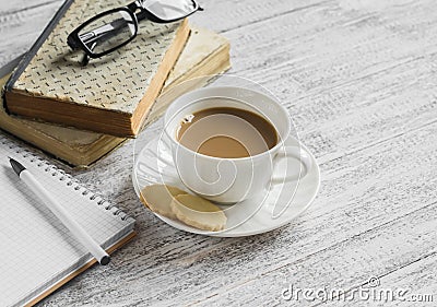 A stack of books, open clean notepad, glasses and a cup of cocoa on a white wooden table. Stock Photo