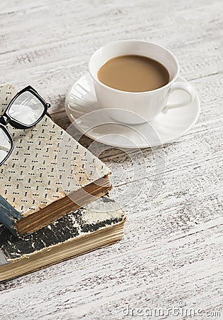 A stack of books, open clean notepad, glasses and a cup of cocoa on a white wooden table. Stock Photo