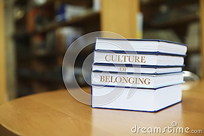 Stack of books with phrase Culture of Belonging on table in library. Space for text Stock Photo