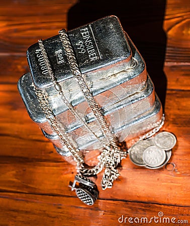 A stack of cast silver bars of different weight, various silver coins and jewelry on a background of mahogany Stock Photo