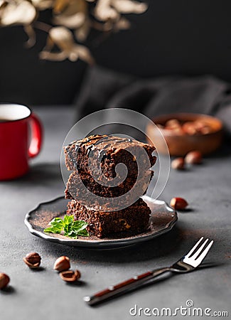 A stack of chocolate brownies with mint and hazelnuts on a dark background with cup of coffee and nuts Stock Photo