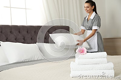Stack of clean towels with flower on bed and chambermaid in hotel room, closeup. Space for text Stock Photo