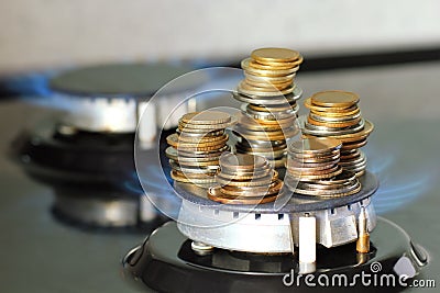 Stack of coins on kitchen stove, blue flame of natural gas burner. Expensive utilities Stock Photo