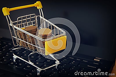 stack of coins in a trolley on a laptop keyboard. make money or shopping online, electronic commerce concept. Stock Photo