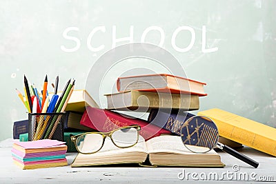 stack of color books, eyeglasses, stationery and magnifying glass on a table and text & x22;School& x22; on green background Stock Photo