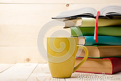 Stack of colorful books, open book and cup on wooden table. Back to school. Copy space Stock Photo