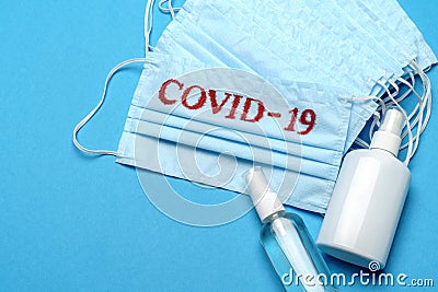 Stack of Disposable blue medical face masks with COVID-19 sign and alcohol hand sanitizer antiseptic on blue background Stock Photo