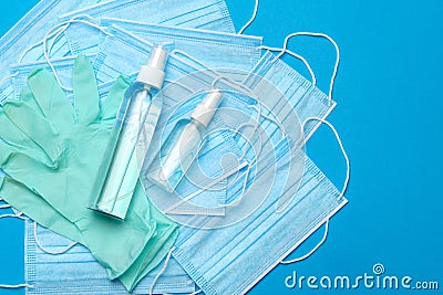 Stack of Disposable blue medical face masks, rubber latex gloves and alcohol hand sanitizer antiseptic on blue Stock Photo