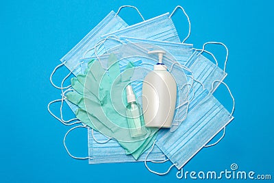 Stack of Disposable blue medical face masks, rubber latex gloves and alcohol hand sanitizer antiseptic on blue Stock Photo