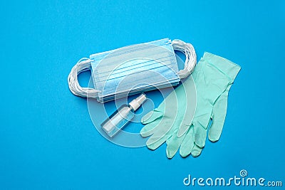 Stack of Disposable blue medical face masks, rubber latex gloves and alcohol hand sanitizer antiseptic on blue Stock Photo