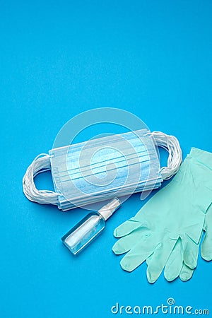 Stack of Disposable blue medical face masks, rubber latex gloves and alcohol hand sanitizer antiseptic on blue Stock Photo