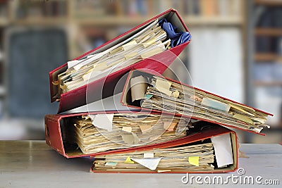 stack of dusty messy file folders with narrow depth of field, blurred office in the back,red tape, bureaucracy,aministration, Stock Photo