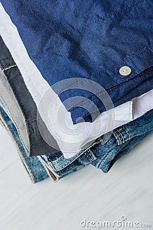 Stack of Folded Cotton Pants Shirts Jeans on White Wood Background Shelf. Eco Fashion Authentic Classic Unisex Style Natural Stock Photo