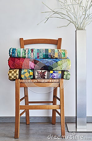 Stack of folded traditional quilts on wooden chair, floor lamp Stock Photo
