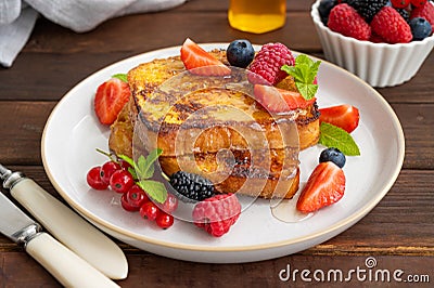 A stack of French toast on a plate with fresh berries, almond petals and honey on a dark wooden background. Delicious breakfast. Stock Photo