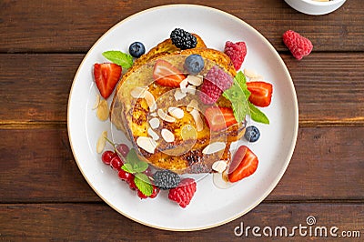 A stack of French toast on a plate with fresh berries, almond petals and honey on a dark wooden background. Delicious breakfast. Stock Photo