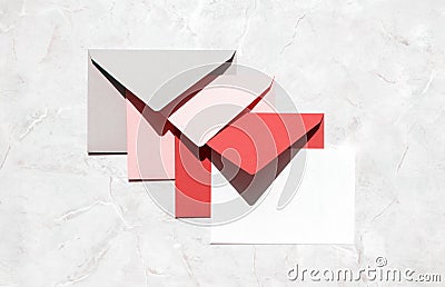 Stack of gray, pink, red mail envelopes and empty white paper card on marble stone table, top view. Bulk mass text mailing Stock Photo