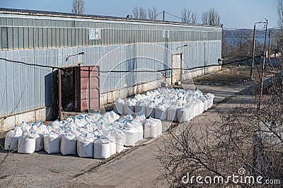 Stack of large bags next to a concealed industrial warehouse outdoors. Cargo handling and storage Stock Photo