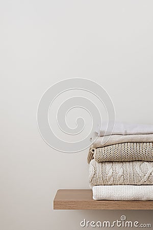 A stack of neatly folded warm knitwear, wool on a wooden shelf and a beige background. Stock Photo