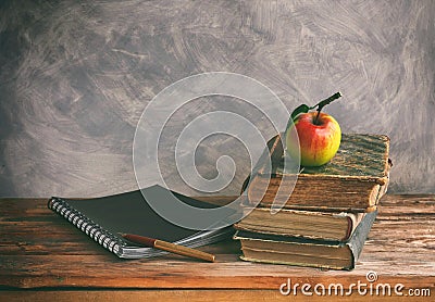 stack of old books, ripe apple, black notebook, fountain pen on wooden table Stock Photo