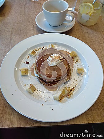 Stack of pancakes covered in maple syrup, sprinkled with nuts, pieces of banana with whipped cream. On a plate in a restaurant Stock Photo