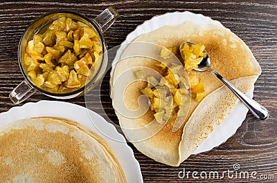 Stack of pancakes in dish, apples with sugar syrup in bowl, pancake filled apples with syrup, teaspoon in plate on table. Top view Stock Photo