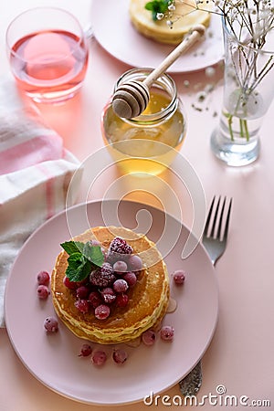 Stack of pancakes with frozen raspberry, red currant and honey on pink background. Selective focus Stock Photo