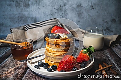 A stack of pancakes with honey, blueberry and strawberry and whip cream on top in plate on wooden table Stock Photo