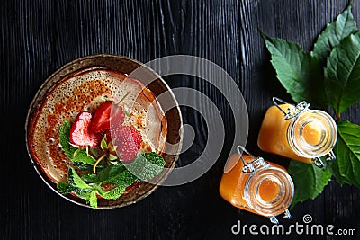 A stack of pancakes with strawberries and mint . Two jars of honey on the table. Photo on a black background. Copy of the space. Stock Photo