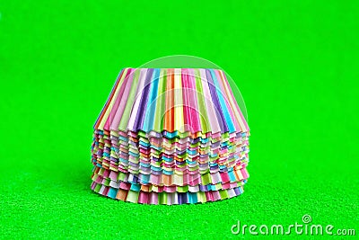Stack Rainbow colored paper baking cups for muffins and cupcakes on a green background minimal creative concept. Space Stock Photo