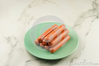 A stack of raw sausages on a green ceramic plate and a white dark table. cloceup Stock Photo