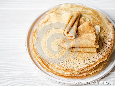 Stack Russian homemade thin pancakes on white plate on wood background. Traditional wheat pancakes for Shrovetide Stock Photo