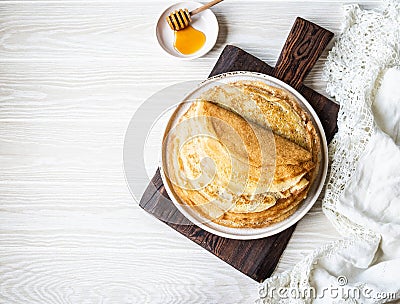 Stack Russian homemade thin pancakes on white plate and wood honey spoon and honey on small white plate. Traditional wheat Stock Photo